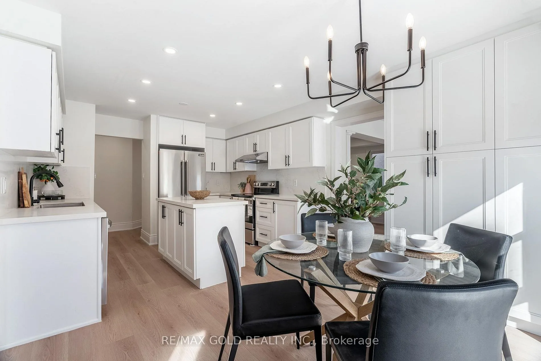 Dining area under a black chandelier, open to a white kitchen