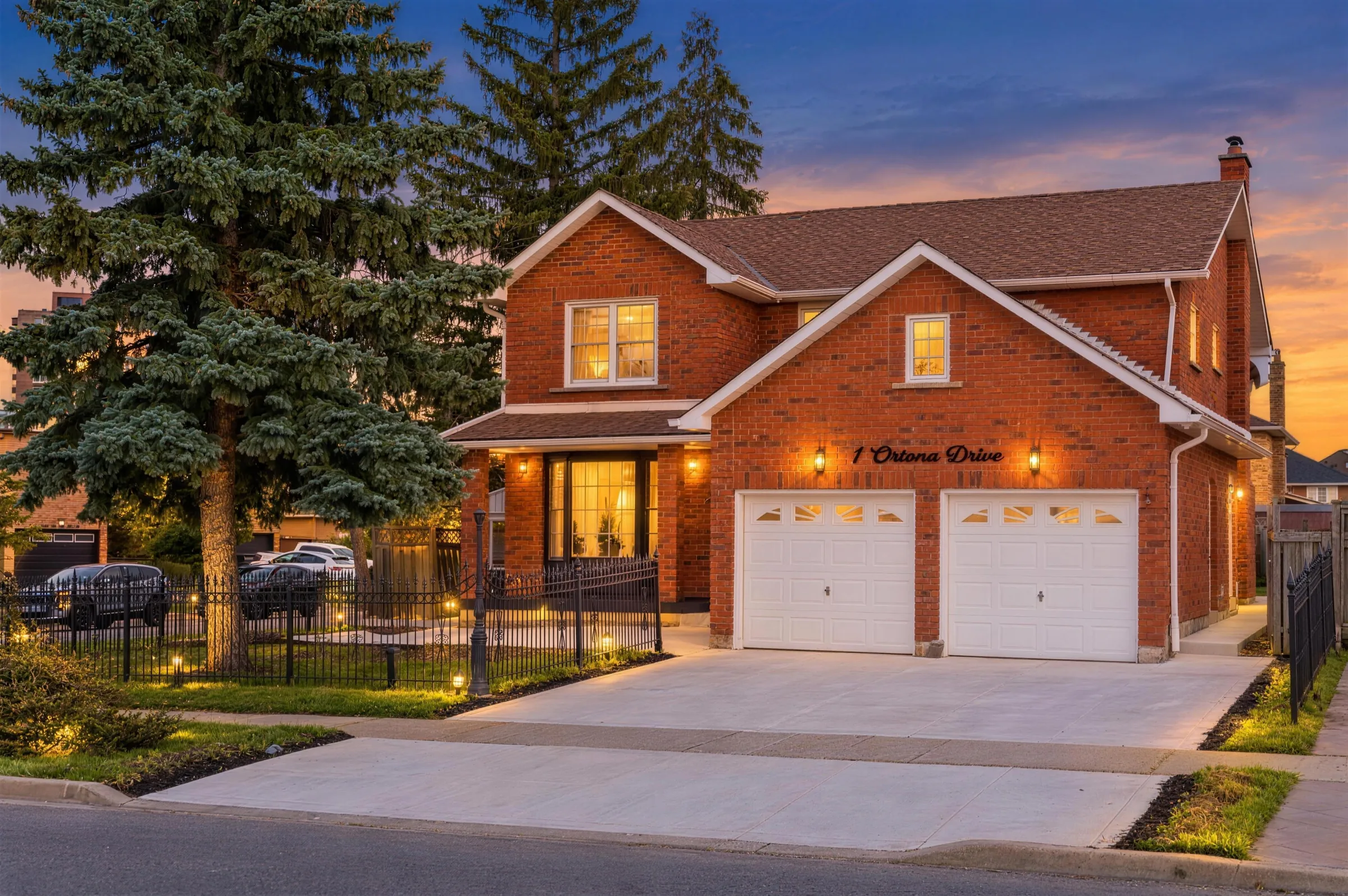 Two-storey red brick home with a double garage, lit up at dusk