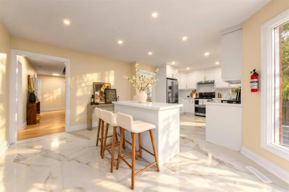Bright kitchen with a white island, bar stools and marble-look floors